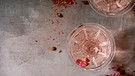 aus der Vogelperspektive fotografiert: zwei Chmapagnerkelche mit Champagner rosé und drei Granatapfelkernen im Glas | Bild: mauritius images / CuboImages / Natasha Breen