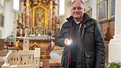 Christian Ertl steht in der Kirche mit einer Taschenlampe neben dem Modell der Kirche St. Peter und Erasmus | Bild: BR / Raimund Lesk 