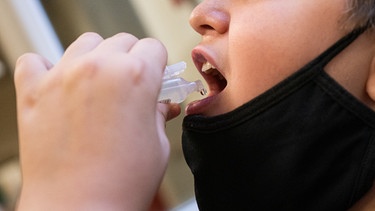 Junge mit abgesetztem Mund-Nase-Schutz setzt Becher zum Gurgeln an | Bild: picture-alliance/dpa