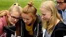 Drei Mädchen prüfen die Einstellung der Kamera. | Bild: BR