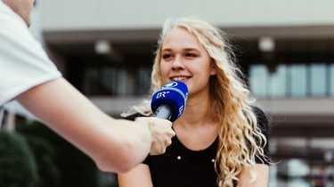 Eine junge Frau wird mit einem BR-Mikrofon interviewt. | Bild: BR/Sylvia Bentele