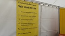 Die Forderungen von "Wir sind Kirche" hängen in einem Zelt.  | Bild: Joseph Röhmel / BR