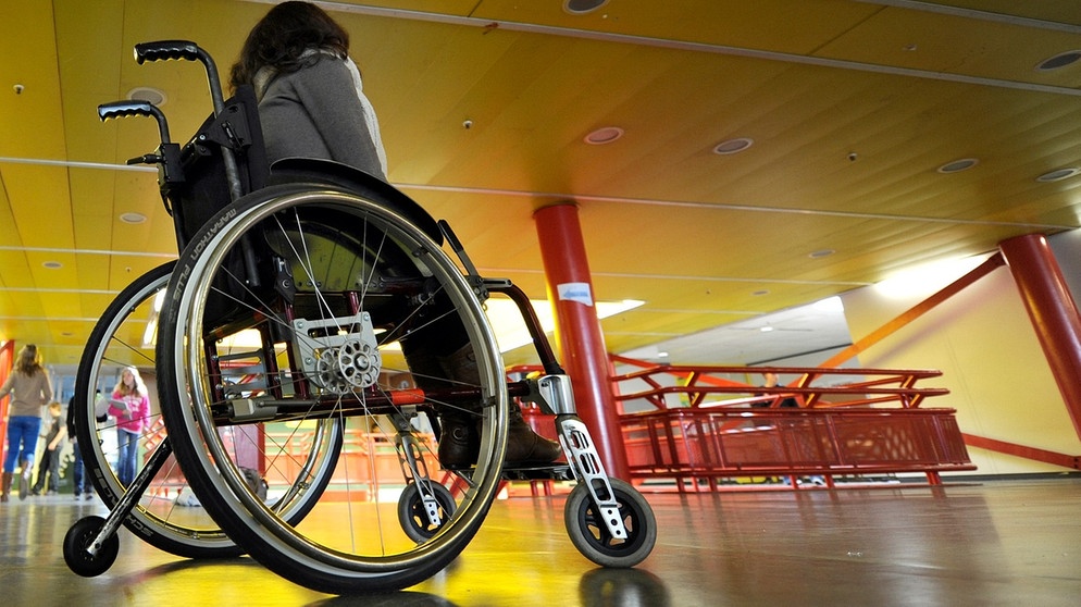 Eine Frau in einem Rollstuhl, von hinten und unten fotografiert. Ihr Gesicht ist nicht zu sehen. | Bild: picture-alliance/dpa