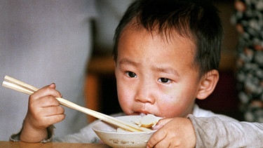 Chongqing (Sichuan): Ein vierjähriger Junge isst mit Essstäbchen aus einer Reisschüssel, aufgenommen in einer Wohnstrasse in der mit 30 Millionen Einwohnern größten Stadt Chinas | Bild: picture-alliance/dpa
