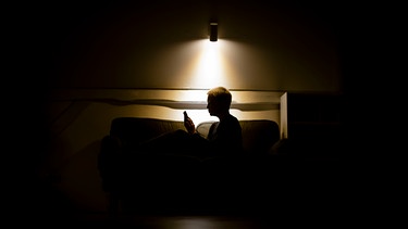 alpha-thema Gespräch: Psyche, Stress und Pandemie | Symbolbild zum Thema Einsamkeit und Isolation: Eine Frau sitzt nachts auf der Couch und schaut in ein Smartphone. | Bild: picture alliance / photothek | photothek/ Thomas Trutschel