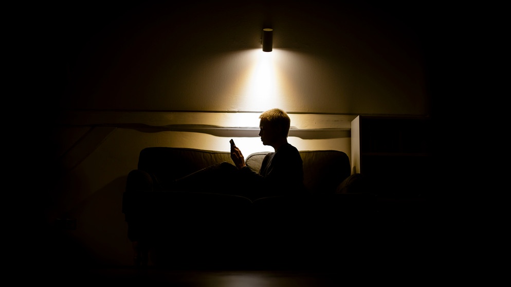 alpha-thema Gespräch: Psyche, Stress und Pandemie | Symbolbild zum Thema Einsamkeit und Isolation: Eine Frau sitzt nachts auf der Couch und schaut in ein Smartphone. | Bild: picture alliance / photothek | photothek/ Thomas Trutschel
