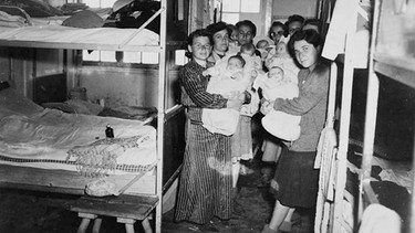 Dieses Foto machten US-Soldaten nach der Befreiung des KZ Dachau am 29. April 1945. Inmitten der Toten trafen sie auf sieben jüdische Frauen mit ihren Säuglingen, die wie durch ein Wunder inmitten des Sterbens überlebt hatten. Marika Novakowá, das Baby vorn rechts auf dem Arm ihrer Mutter Eva, will 65 Jahre später wissen, wie das möglich war. | Bild: © WDR/WDR/USHMM Washington, honorarfrei - Verwendung gemäß der AGB im engen inhaltlichen, redaktionellen Zusammenhang mit genannter WDR-Sendung bei Nennung "Bild: WDR/WDR/USHMM Washington" (S1). WDR Presse und Information/Bildkommunikation, Köln, Tel: 0221/220 -7132 oder -7133, Fax: -777132, bildkommunikation@wdr.de.