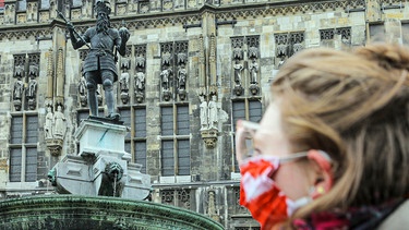 Eine Frau geht auf dem Aachener Marktplatz mit einem Mund-Nasen-Schutz am Karlsbrunnen vorbei.  | Bild: dpa-Bildfunk/Ralf Roeger
