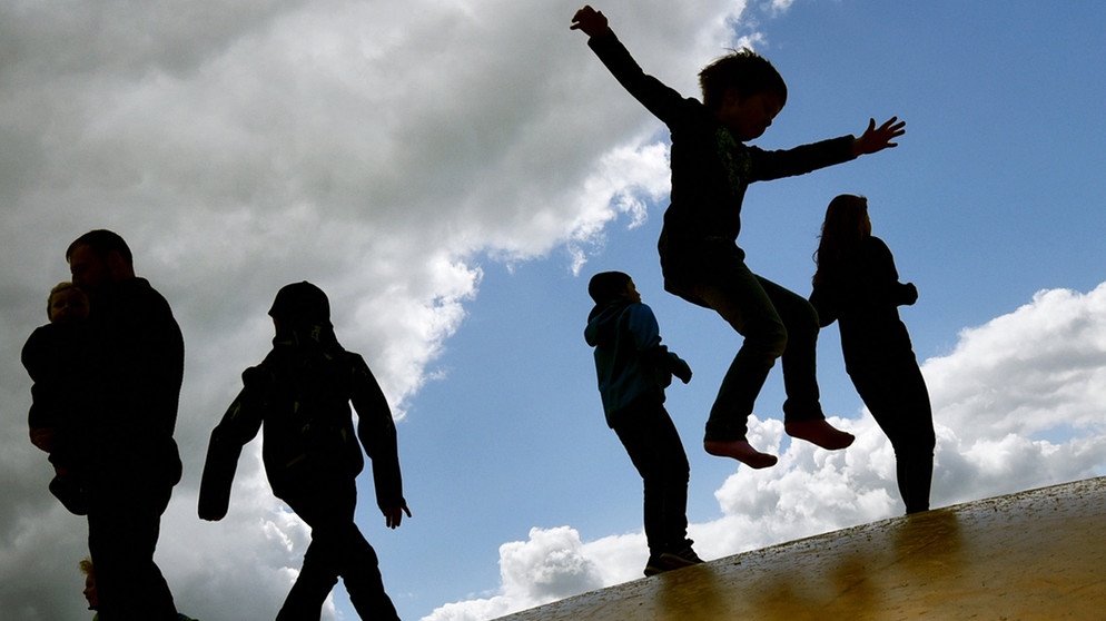 Kinder springen auf einer Hüpfburg und heben sich dabei als Schatten vom Himmel ab. | Bild: dpa-Bildfunk/Ralf Hirschberger