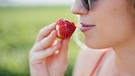 Eine Frau mit Sonnenbrille isst eine Erdbeere. | Bild: BR/Julia Müller