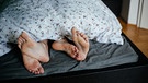 Ein Pärchen liegt im Bett, die Füße schauen aus der Bettdecke hervor. | Bild: BR/Julia Müller