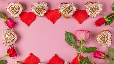 Symbolbild für die Liebe: ein Rahmen aus herzförmigen Muffins, roten Herzen und Rosen | Bild: picture alliance / imageBROKER / Lucas Seebacher