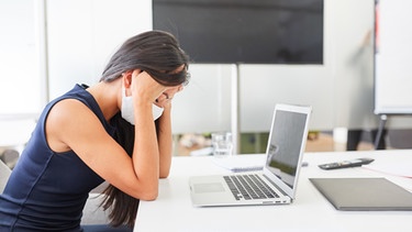 Business Frau mit Gesichtsmaske wegen Covid-19 sitzt mit Burnout durch Überlastung am Computer | Bild: picture-alliance/dpa