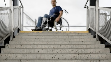 Ein Rohlstuhlfahrer steht vor einer Treppe.  | Bild: stock.adobe.com/gradt