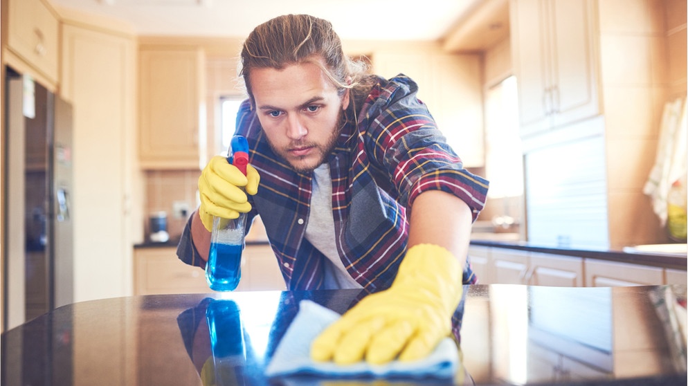 Ein junger Mann putzt sorgfältig einen Küchentisch. Wo befinden sich im Alltag die meisten Keime? Wir erklären euch bei welchen Gegenständen ihr aufpassen solltet, wo es Entwarnung gibt und wie ihr Keime zuverlässig loswerdet.  | Bild: Wochit/ Getty Images