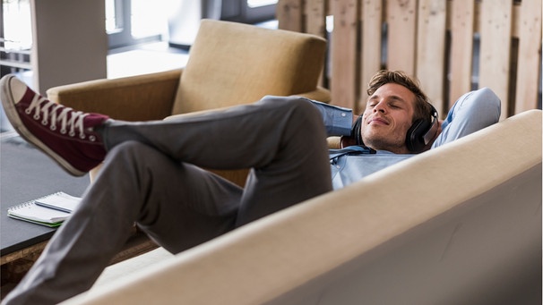 Ein junger mann liegt auf der Couch und macht eine Pause. Wir erklären euch, warum regelmäßige Pausen im Alltag wichtig sind, wie oft ihr eine Auszeit einlegen solltet und wie ihr euch am besten in eurer freien Zeit erholen könnt.   | Bild: Wochit/Getty Images 
