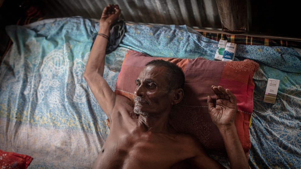 Mann auf seinem Bett in seiner Hütte, neben dem Kissen liegen seine Medikamente, er ist fast blind und kann nur schwer atmen, da er sein Leben lang salzhaltiges und arsenverseuchtes Trinkwasser zu sich genommen hat, Mongla, Sundarbans, Bangladesch, Asien | Bild: picture alliance / imageBROKER | Florian Bachmeier