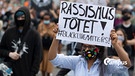 "Rassismus tötet" steht auf dem Plakat einer Frau, die sich auf der Hauptwache in Frankfurt an einer Kundgebung gegen Polizeigewalt beteiligt. Anlass der Demonstration ist der gewaltsame Tod eines Mannes in den USA durch die Polizei. Symbolbild mit Campus Logo | Bild: picture alliance/dpa | Boris Roessler