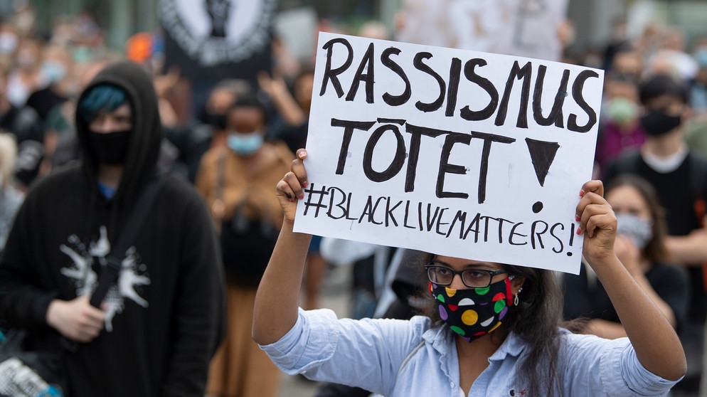 "Rassismus tötet" steht auf dem Plakat einer Frau, die sich auf der Hauptwache in Frankfurt an einer Kundgebung gegen Polizeigewalt beteiligt. Anlass der Demonstration ist der gewaltsame Tod eines Mannes in den USA durch die Polizei. Symbolbild  | Bild: picture alliance/dpa | Boris Roessler