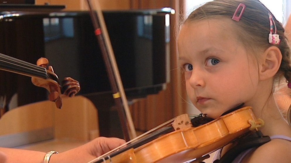 Yamina lernt in der Musikschule der Hofer Symphoniker Geige spielen. Sie bekommt gerade die richtige Haltung des Bogens gezeigt. | Bild: BR