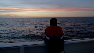 Mann schaut auf das Meer | Bild: picture alliance / ASSOCIATED PRESS | Luca Bruno
