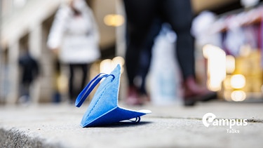 Eine blaue FFP2-Maske liegt auf einem Gehweg in der Münchner Innenstadt mit Campus Logo | Bild: picture alliance/dpa | Matthias Balk