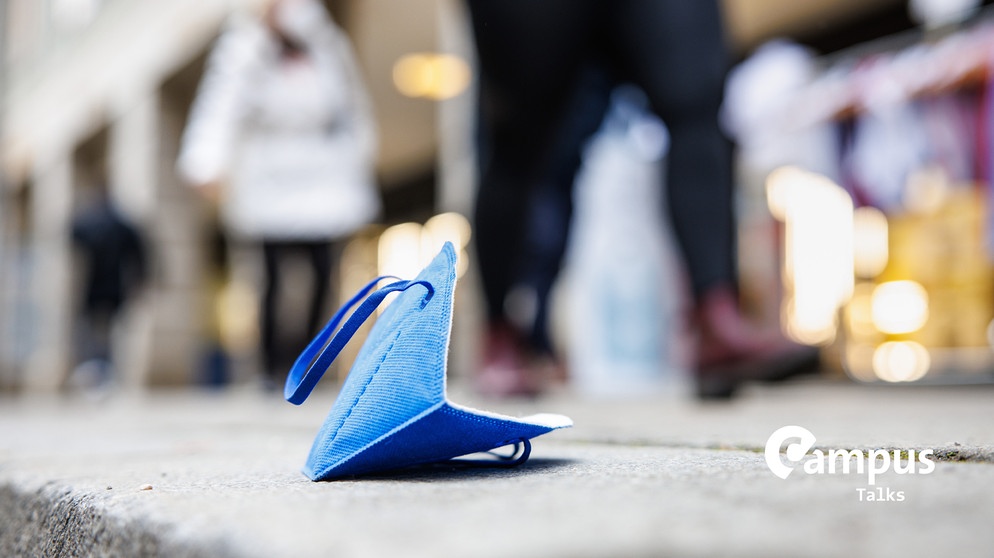 Eine blaue FFP2-Maske liegt auf einem Gehweg in der Münchner Innenstadt mit Campus Logo | Bild: picture alliance/dpa | Matthias Balk