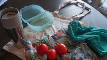 Auf einem Tisch liegen Stoffbeutel, Gemüsenetz, eine Tupperdose, eine Thermoskanne und Tomaten. | Bild: BR/Leon Baatz
