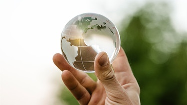 Hand hält eine Weltkugel aus Glas. Umwelt und Klimaschutz Konzept | Bild: picture alliance / CHROMORANGE | Michael Bihlmayer
