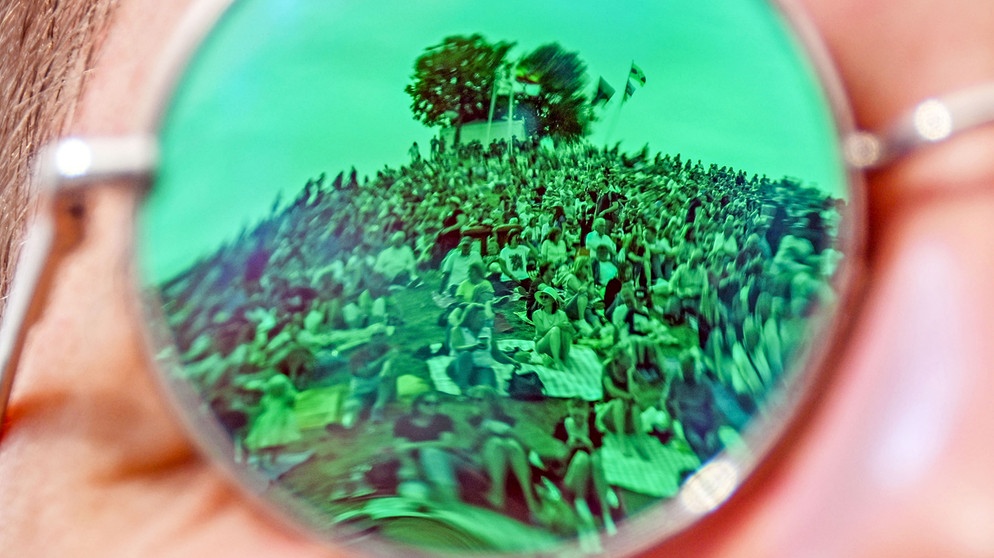 In der Sonnenbrille eines Besuchers des Open-Air-Festival «Das Fest» spiegeln sich Festivalbesucher wider.  | Bild: picture alliance/dpa | Uli Deck