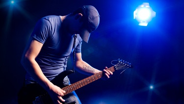 Mann spielt Gitarre auf einer Bühne, beleuchtet von einem Scheinwerfer | Bild: colourbox.com