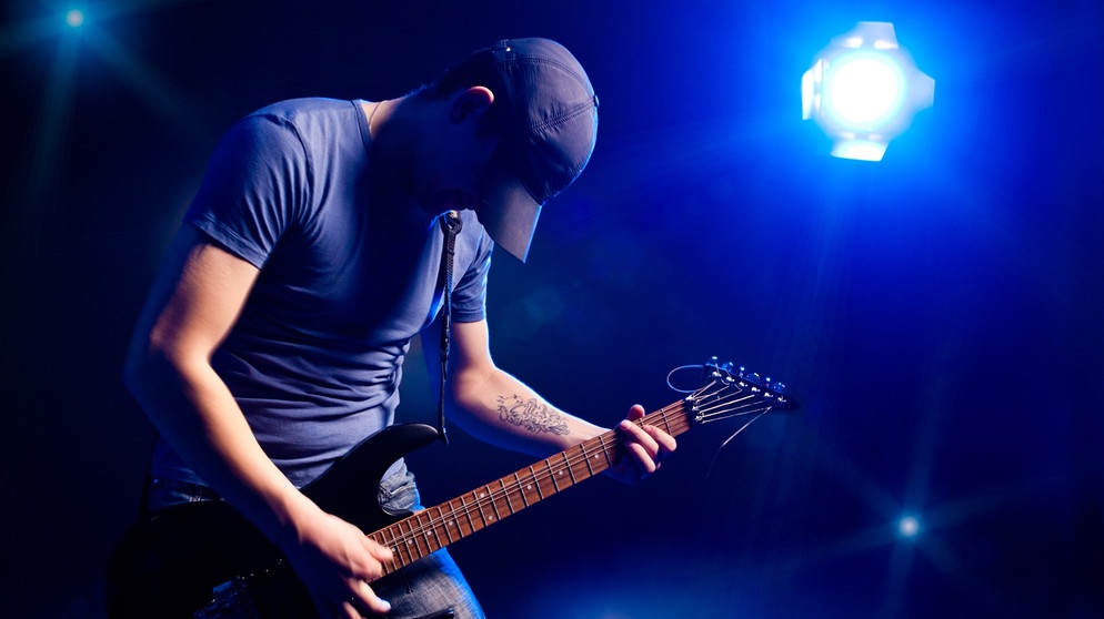 Mann spielt Gitarre auf einer Bühne, beleuchtet von einem Scheinwerfer | Bild: colourbox.com