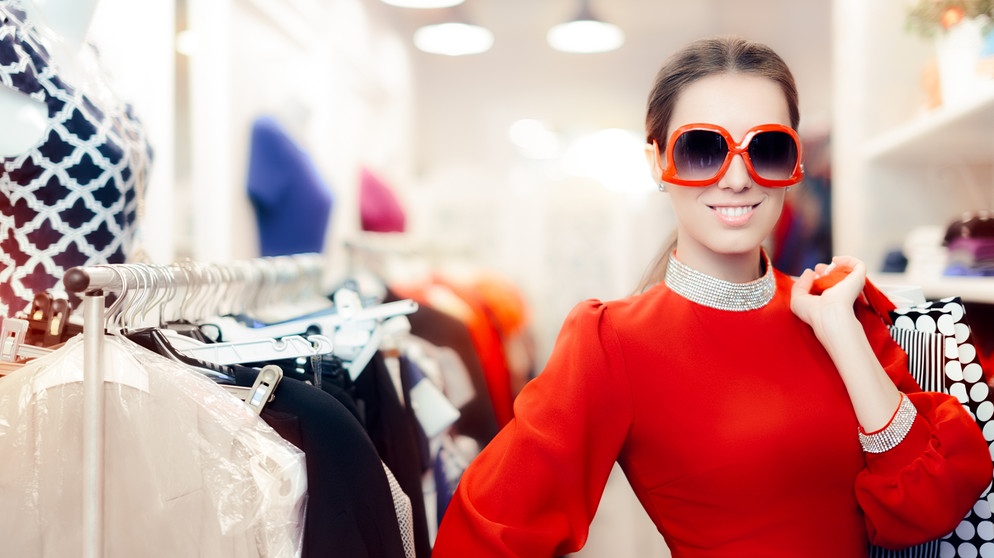 Frau beim Shoppen in einem Geschäft. Sie trägt ein knallrotes Kleid und hat eine rot-umrandete Sonnenbrille auf. | Bild: colourbox.com