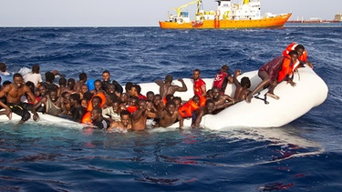 Flüchtlinge sitzen auf dem Mittelmeer in einem sinkenden Schlauchboot.  | Bild: dpa-Bildfunk/Ong Sos Mediterranee