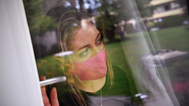 Frau hinter einer Scheibe mit Mund-Nasen-Schutz. | Bild: Sven Simon/ Picture Alliance