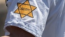 "Ungeimpft" steht auf dem einem Juden-Stern-Binde aus dem 3.Reich nachempfundenen Sticker am Arm eines Mannes auf einer Demonstration. | Bild: picture alliance/dpa | Boris Roessler