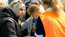 Helferin in orangefarbener Weste mit einer Mutter | Bild: picture-alliance/dpa