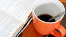 Eine Tasse mit Kaffee neben einem aufgeschlagenen Buch | Bild: colourbox.com