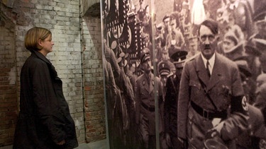Eine Frau steht vor einem großformatigen Foto von Adolf Hitler auf dem Reichsparteitag | Bild: picture-alliance/dpa