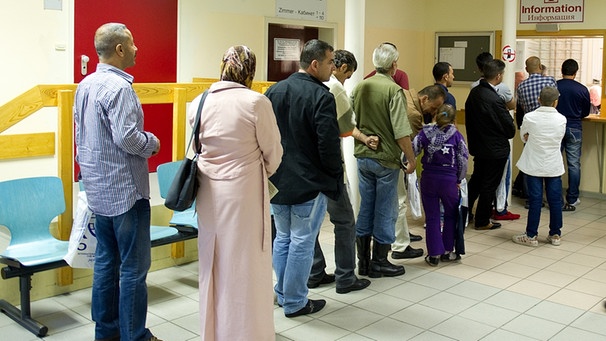 Asylbewerber stehen in einer Schlange an einer Informationsstelle | Bild: picture-alliance/dpa