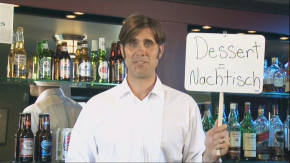 Ein Ober hält ein Schild mit dem Ausdruck Dessert =Nachtisch hoch | Bild: Bayerischer Rundfunk