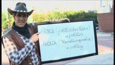 Der Cowboy mit einem Schild und den Bedeutungen von Politik im Englischen | Bild: Bayerischer Rundfunk