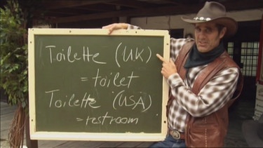 Der Cowboy mit einer Tafel und den Wörtern für Toilette im amerikanischen und britischen Englisch | Bild: Bayerischer Rundfunk