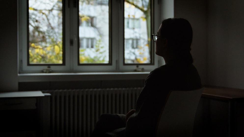 Person in dunklem Raum blickt aus dem Fenster | Bild: Bayerischer Rundfunk 2024