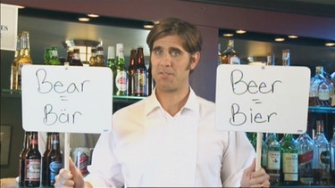 Ein Kellner mit zwei Schildern, darauf bear (Bär) und beer (Bier) | Bild: Bayerischer Rundfunk