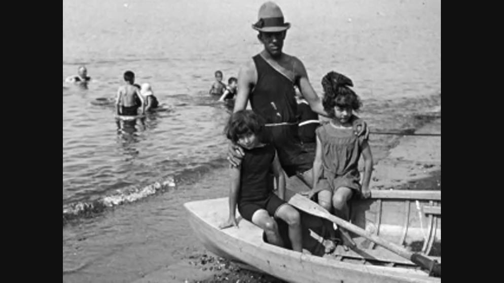 Mann mit zwei Kindern im Boot, im Hintergrund badende Kinder | Bild: Bayerischer Rundfunk