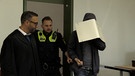 Polizisten und Angeklagter mit Aktenordner vor Gesicht betreten Gerichtssaal | Bild: Bayerischer Rundfunk 2023