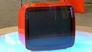 Leuchtend roter tragbarer Fernseher von Grundig, dessen Bedienfläche auf der Rückseite des Gerätes versteckt ist. So erscheint die Front dieses futuristisch anmutenden Fernsehers glatt und elegant. Geschätzter Wert: 50 Euro  | Bild: Bayerischer Rundfunk