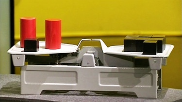 Eine Waage im Gleichgewicht mit unterschiedlichen Objekten; links Quader und Zylinder, rechts nur Quader | Bild: BR