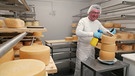 Ein Mitarbeiter steht an einem Käselaib im Reiferaum der Käserei. | Bild: Bayerischer Rundfunk 2024